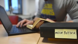 Ein Texter schreibt an seinem Laptop einen gedruckten Roman mit seinen Lieblingscharakteren weiter.