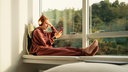 Eine Frau sitzt auf einer Fensterbank und hört über Kopfhörer Musik.