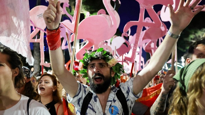 Ein Mann mit Blumenkranz auf dem Kopf zwischen anderen Demonstrant:innen bei der "Flamingo-Revolution" in Albanien.