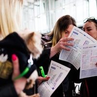 Eine Besucherin trägt einen Hund auf dem Arm, während andere im Hintergrund im Ausstellungsplan blättern, bei der Jobmesse für Geflüchtete "FuTog Berlin".
