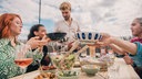 Menschen sitzen auf einer Dachterasse und essen gemeinsam.