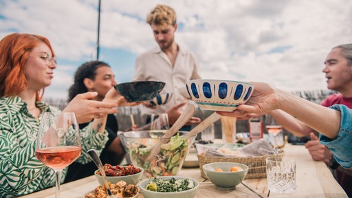 Menschen sitzen auf einer Dachterasse und essen gemeinsam.
