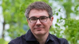 Die Porträtaufnahme des Autors und Journalisten Hauke Friederichs zeigt ihn mit kurz geschnittenem, leicht ergrautem Haar, schwarzer Brille und dunklem Hemd.