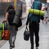 Zwei Menschen mit schwerem Outdoor-Reisegepäck auf den Schultern gehen über den Bahnsteig zu einem Zug.