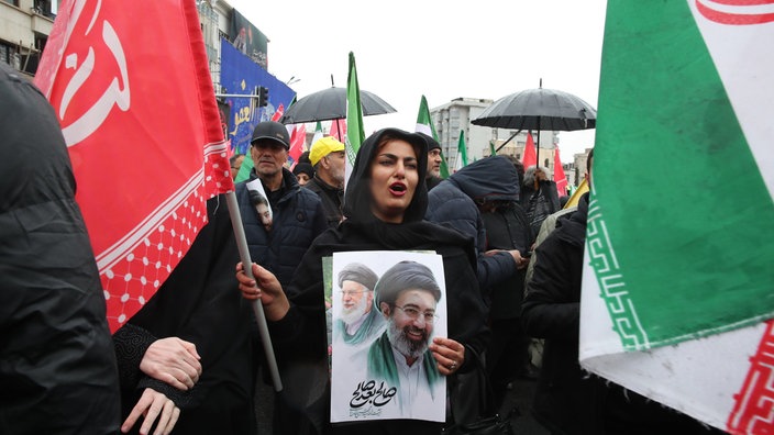 Eine Frau hält ein Plakat mit den Konterfeis des getöteten iranischen Obersten Führers Ajatollah Ali Chamenei (l) und seines Sohnes, des neuen iranischen Obersten Führers Modschtaba Chamenei, während einer Kundgebung zum jährlichen Kuds-Tag 