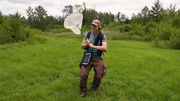 Naturschützer Karsten Cieslik steht mit einem großen Schmetterlingsnetz mitten im Grünen.