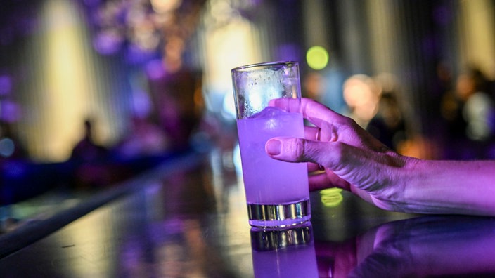 Eine Frau greift nach einem Glas mit einem Cocktail in einem Club