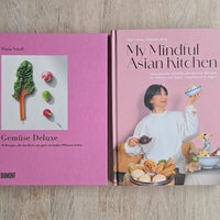 Die beiden rosafarbenen Kochbücher "Gemüse Deluxe" und "My Mindful Asian Kitchen" liegen auf einem gräulichen Holztisch.