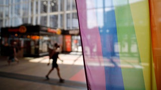 Vor dem Infoschalter der Deutschen Bahn im Kölner Hauptbahnhof stehen Regenbogenflaggen. 