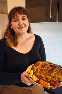 Junge Frau hält einen Teller, auf dem sich Challah-Brot befindet, in der Hand. 