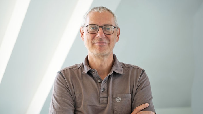 Das Porträt zeigt Matthias Bernt mit kurzen Haaren, dunkler Brille und freundlichem Lächeln vor einem hellen, lichtdurchfluteten Hintergrund.