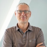 Das Porträt zeigt Matthias Bernt mit kurzen Haaren, dunkler Brille und freundlichem Lächeln vor einem hellen, lichtdurchfluteten Hintergrund.
