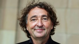 Die Porträtaufnahme zeigt Michael Horeni mit lockigem Haar und einem freundlichen Lächeln.