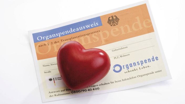 Ein roter herzfärmiger glatter Stein liegt auf einem Organspendeausweis