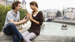 Mann überreicht Frau am Ufer der Seine in Paris eine Miniausgabe des Eiffelturms. 