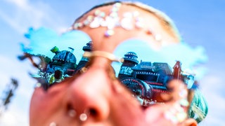 Die Bühne Bills Factory spiegelt sich in den Gläsern einer herzförmigen Sonnenbrille einer Festivalbesucherin.