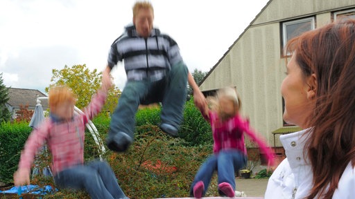 Eine Frau schaut ihren Pflegekindern im Garten beim Trampolinspringen zu.