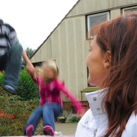 Eine Frau schaut ihren Pflegekindern im Garten beim Trampolinspringen zu.