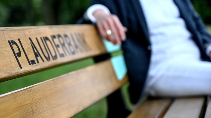 Eine Frau sitzt auf einer Bank mit der Aufschrift "Plauderbank"