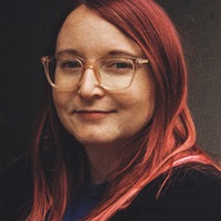Die Porträtaufnahme zeigt Ramona Wuttig mit roten Haaren, Brille und freundlichem Lächeln.
