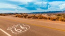 Die legendäre U.S. Route 66 bei Amboy in Kalifornien: Das Route-66-Zeichen auf dem Asphalt, im Hintergrund zieht ein langer Güterzug durch die Mojave-Wüste.