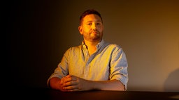 Sebastian Majstorovic, Mitbegründer des Datenrettungsprojekt "Data Rescue Project" sitzt mit gefalteten Händen an einem Tisch in orangenem Licht