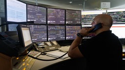 Ein Fahrdienstleiter spricht am Zugfunk mit einem Lockführer, während er ein elektronisches Stellwerk bedient. 