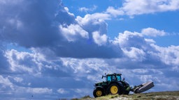 Ein Traktor ist mit einem Mähbalken vor einer dunklen Wolkenkulisse auf einer Wiese unterwegs. 