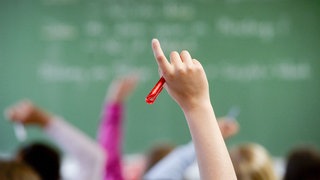 Nahaufnahme des Arms einer Schülerin oder eines Schülers, der sich im Klassenzimmer meldet.