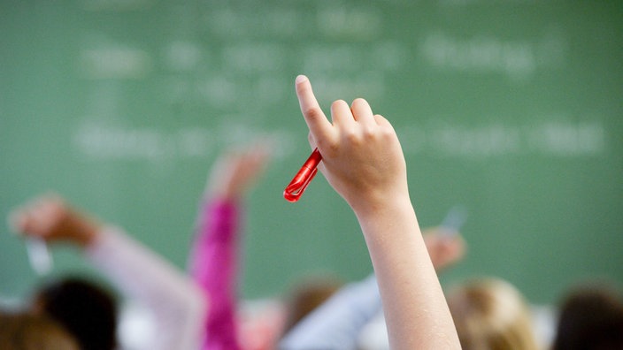 Nahaufnahme des Arms einer Schülerin oder eines Schülers, der sich im Klassenzimmer meldet.