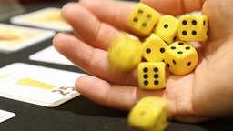 Die Würfel des Spiels "Käse Würfeln" werden von einer Spielerin auf den Tisch gerollt. 