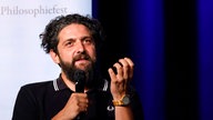 Porträt Aladin El-Mafaalani diskutierend bei einer Veranstaltung, im Hintergrund der Schriftzug 'Philosophiefest'