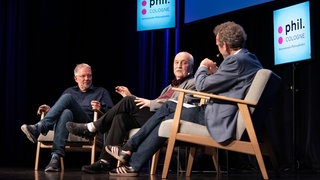 Wolfgang Palaver und Arnd Henze sitzen auf Stühlen auf der Bühne der phil.COLOGNE