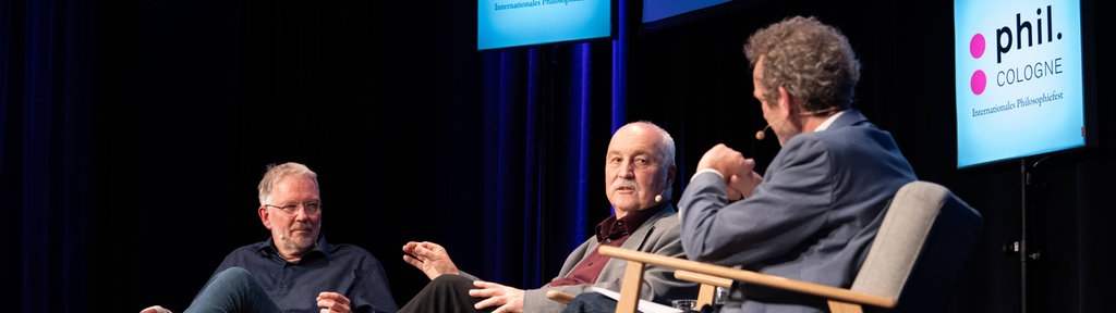 Wolfgang Palaver und Arnd Henze sitzen auf Stühlen auf der Bühne der phil.COLOGNE