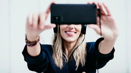 Frau mit Kopfhörern hält ihr Handy vors Gesicht