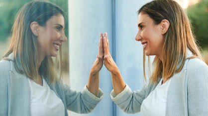 Eine Frau steht vor einer Fensterscheibe und spiegelt sich darin
