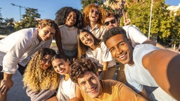 Eine multikulturelle Freundesgruppe lacht und blickt gemeinsam in die Kamera