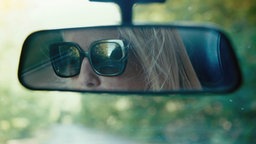Man sieht eine Frau, die in den Rückspiegel ihres Autos blickt