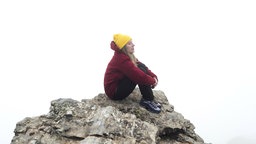 Frau sitzt auf einem Fe3lsen und im Hintergrund ist Nebel