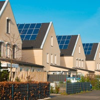 EineReihe neuer Einfamilienhäuser mit Solarpaneelen auf den Dächernvor strahlend blauem Himmel