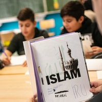 Ein Schüler öffnet in einem Klassenraum einen Schnellhefter mit einem selbst gestalteteten Deckblatt für das Fach Islamunterricht.