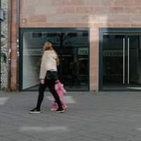 Frau mit Kind geht an zwei leeren Schaufenstern in einer kargen Fassade vorbei