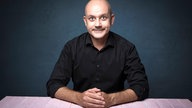 Frank Fischer sitzt an einem Tisch und schaut interessiert in die Kamera, Foto: Oli Haas