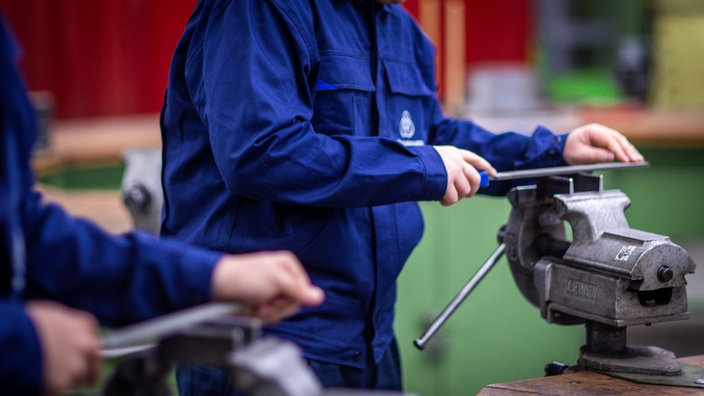 Lehrlinge arbeiten mit einer Metallfeile an Schraubstöcken in einer Lehrwerkstatt