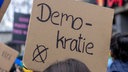 Symbolbild: Bei einer Demonstration sind auf einem Schild der Schriftzug "Demokratie" und ein Wahlkreuz zu sehen.