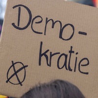 Symbolbild: Bei einer Demonstration sind auf einem Schild der Schriftzug "Demokratie" und ein Wahlkreuz zu sehen.