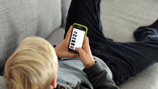 Eine Junge liegt auf einer Couch und schaut auf sein Smartphone