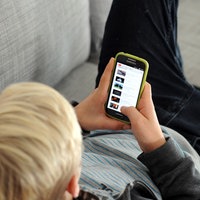 Eine Junge liegt auf einer Couch und schaut auf sein Smartphone
