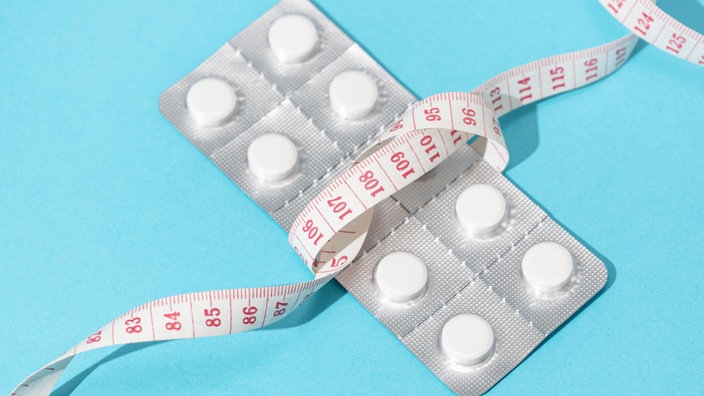 Eine Blisterverpackung mit Abnehmtabletten, umgeben von einem Maßband.