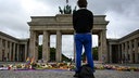 in Mensch steht vor dem Brandenburger Tor, wo nach dem Anschlag auf den CSD Blumen, Kerzen und persönliche Botschaften niedergelegt worden sind.